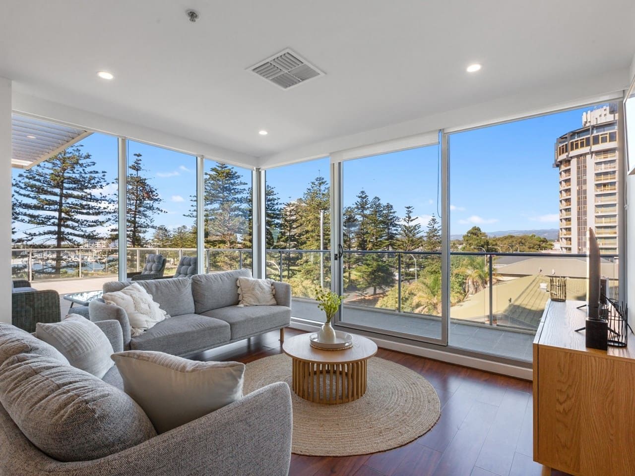 A modern living room with a grey sectional sofa, a round coffee table, and a view of a cityscape through large windows.