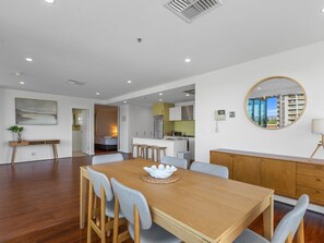 Un espace repas moderne avec une table et des chaises en bois, une cuisine en arrière-plan et une vue par la fenêtre.
