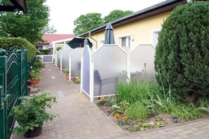 Ein Weg führt zu einem Gebäude mit einer gelben Fassade, umgeben von einem grünen Zaun und Blumentöpfen.