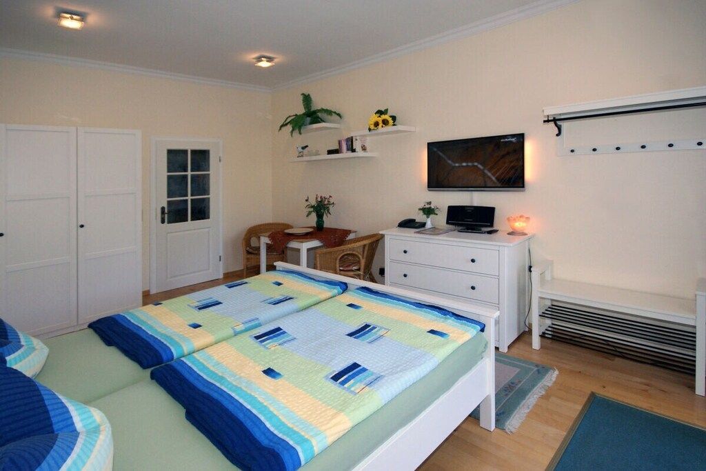 Un dormitorio con cama, escritorio, silla, televisor y estante con adornos.