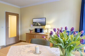 A hotel room with a bed, a desk with a lamp, a television, a vase of flowers, and a door. - At Schloonsee, Apartment C-2 (Seebad Heringsdorf)