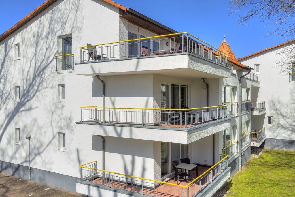 A multi-story residential building with balconies, outdoor seating, and a clear sky.