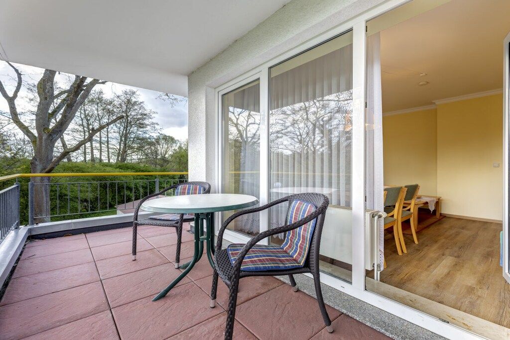 Un balcon avec une table et des chaises, une porte-fenêtre coulissante et une vue sur les arbres et le ciel.