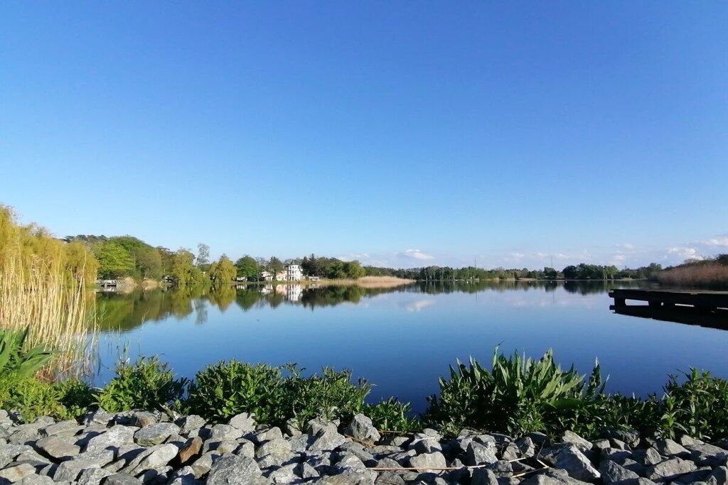 Un lac paisible, avec un mur de pierres au premier plan et un ciel bleu dégagé.
