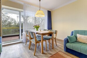A dining area with a table and chairs, a sofa, and a view through a glass door. - At Schloonsee, Apartment C-2 (Seebad Heringsdorf)