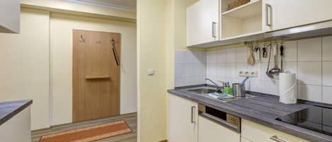 A kitchen with a wooden door, white cabinets, a countertop, and a hanging rack with kitchen utensils.