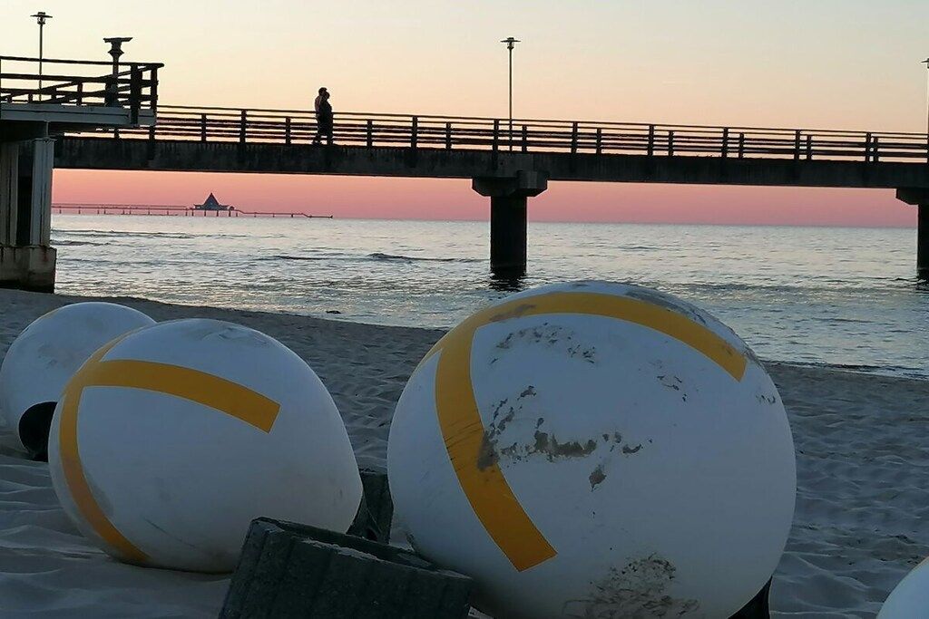 A beach with volleyballs, a pier, and a sunset.