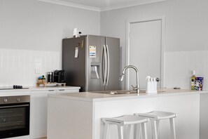 Eine moderne Küche mit einem Edelstahl-Kühlschrank, einem Einbauofen, einer Spüle mit modernem Wasserhahn und zwei weißen Barhocker.
