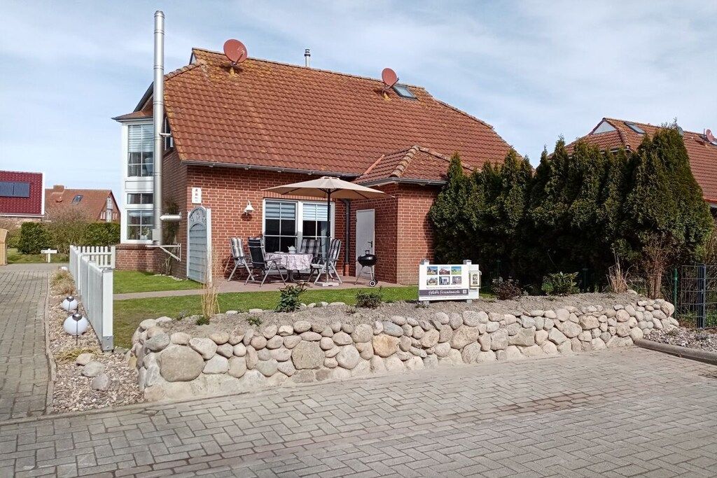 Une maison à deux étages, avec une façade en briques, un toit en tuiles et un patio aménagé avec du mobilier d’extérieur.