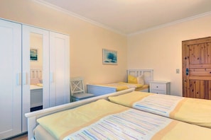 A bedroom with two beds, a wardrobe, a chair, a bedside table, and a door. - House by the Forest Apartment 3 (Seebad Ahlbeck)
