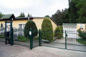 Una propiedad cerrada con valla verde, un edificio pequeño con techo inclinado y setos bien recortados.