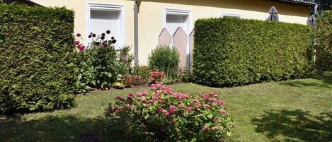 A yellow building with white shutters, surrounded by well-maintained hedges and flowering plants.