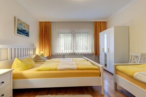Un dormitorio con cama, mesitas de noche, armario y ventana con cortinas.