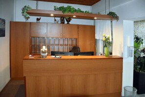 Un mostrador de recepción de madera con una vitrina de vidrio, un monitor Benq y un jarrón con flores.