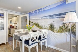 A dining area with a table and chairs, a lamp, and a beach mural on the wall. - Richard House Apt. 3 (Seebad Ahlbeck)