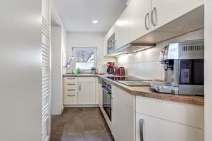 A modern kitchen with white cabinetry, a built-in oven, a coffee machine, and a window with a view. - Richard House Apt. 3 (Seebad Ahlbeck)