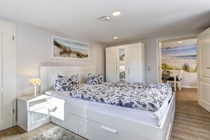 A bedroom with a large bed, bedside tables, a nightstand, and a view of the beach through an open door. - Richard House Apt. 3 (Seebad Ahlbeck)