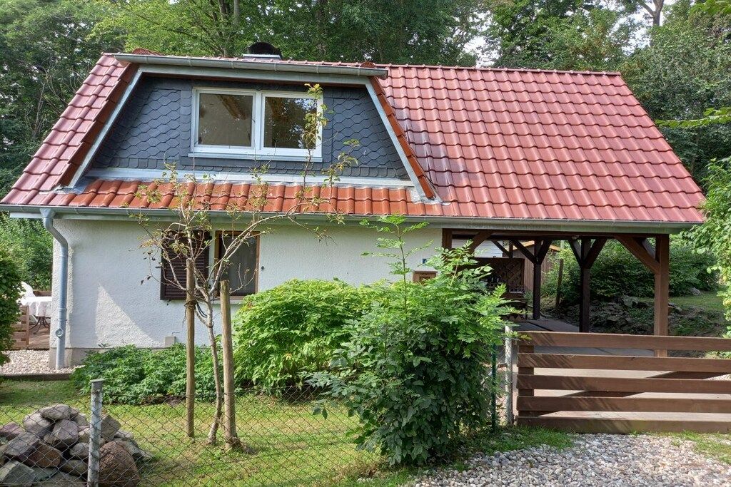 Ein kleines Haus mit rotem Ziegeldach, einer Holzveranda und einem eingezäunten Garten.