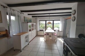 A kitchen with a stove, a dining table with chairs, a white cabinet, and a window with curtains. - in the Recknitz valley (Ahrenshagen- Daskow)