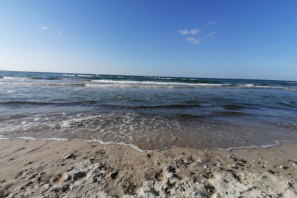 Ein Strand mit ankommenden Wellen, feinem Sand und einem klaren Himmel.