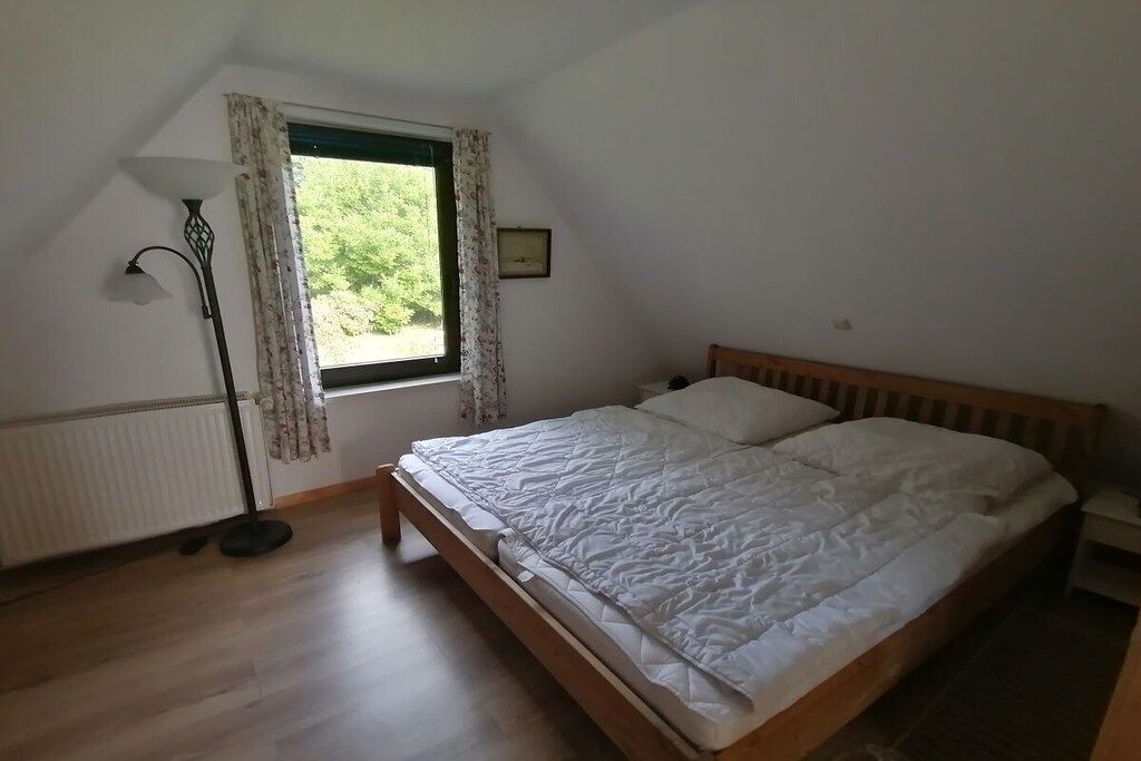 A bedroom with a wooden bed, a window with curtains, a floor lamp, and a radiator.