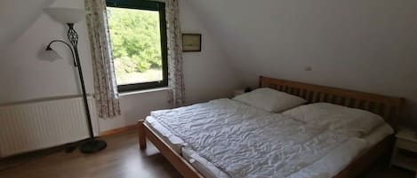 Ein Schlafzimmer mit einem hölzernen Bett, einem Fenster mit Vorhängen, einer Stehlampe und einer Heizung.