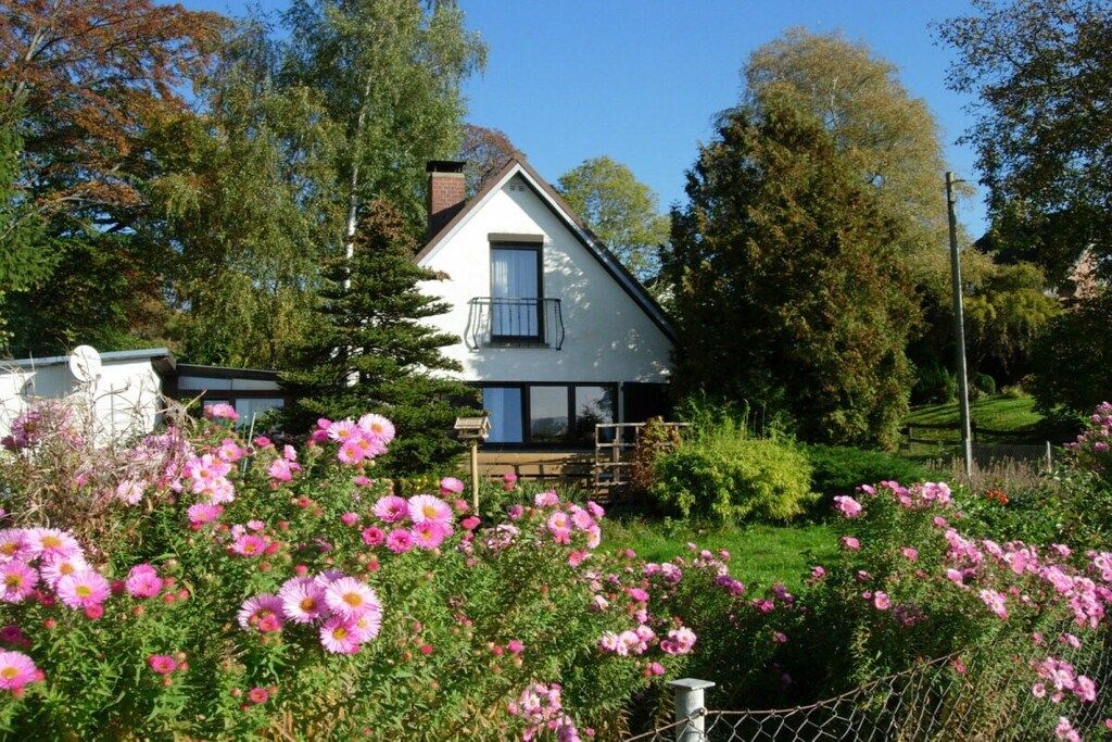 A house with a white exterior, a balcony, and a garden with pink flowers.
