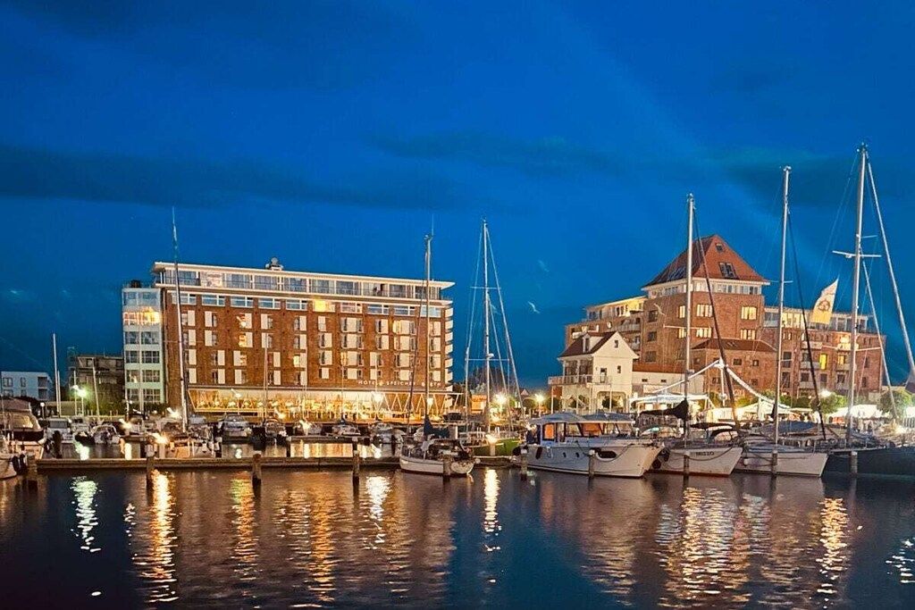 Una marina con varios barcos amarrados, un hotel con un techo rojo llamativo y un edificio moderno con grandes ventanales.