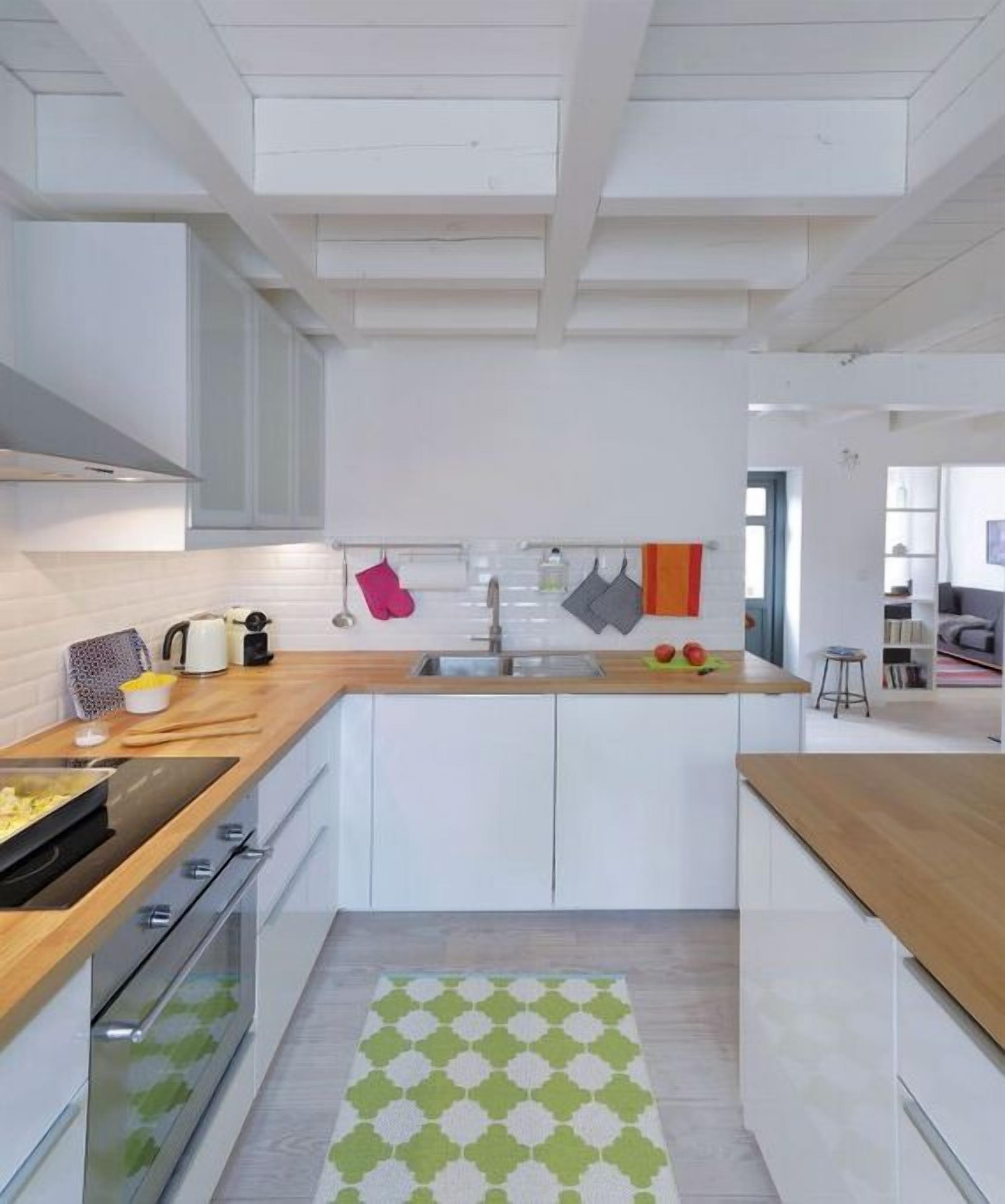 A modern kitchen with white cabinetry, a wooden countertop, and a patterned rug.