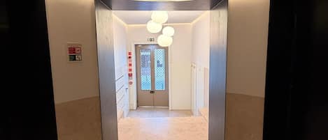 A modern hallway with a curved ceiling, a central light fixture, and a door at the end.