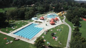 A large swimming pool surrounded by grass, a water slide, and a building with a red roof.