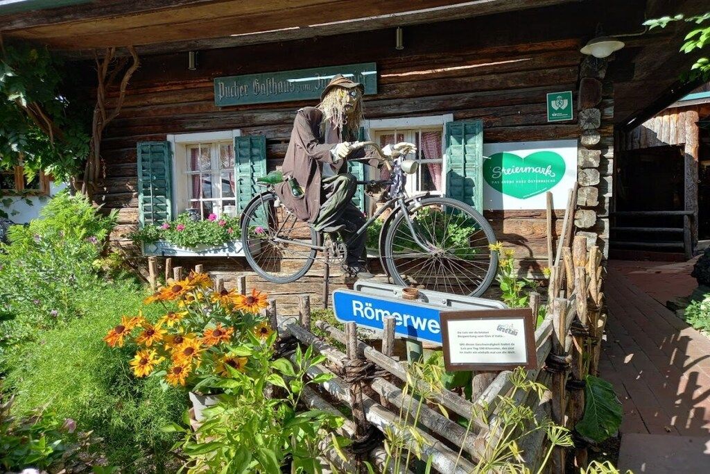 Une construction rustique en bois, avec un vélo et une silhouette vêtue d’un costume d’épouvantail.