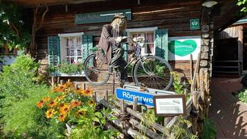 Un edificio rustico in legno con una bicicletta e una persona vestita da spaventapasseri.