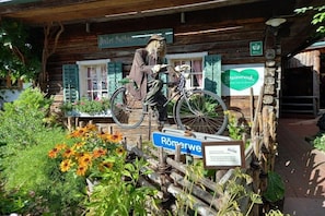 A rustic wooden building with a bicycle and a figure dressed as a scarecrow.