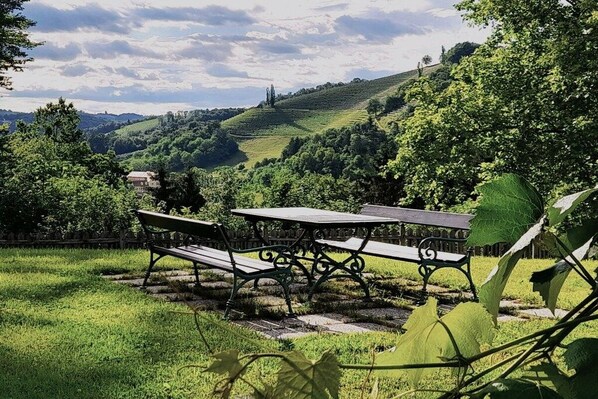 A park with two picnic tables and benches, surrounded by lush greenery and hills.