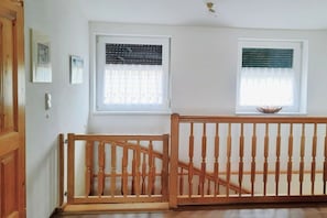 A room with two windows, a wooden railing, and a door.