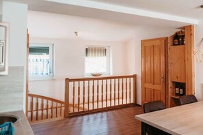 A room with a wooden staircase, a dining table, and a wooden cabinet with bottles.