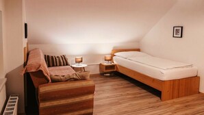 A small, cozy bedroom with a wooden bed, a single bedside table with a lamp, a wooden bench, and a radiator.