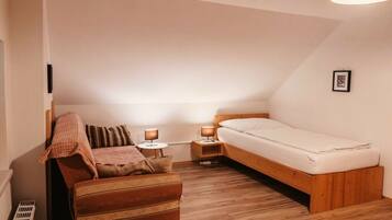 A small, cozy bedroom with a single bed, a wooden nightstand, a bedside table with a lamp, and a cushioned bench.