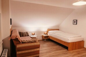 A small, cozy bedroom with a wooden bed, a single bedside table with a lamp, a wooden bench, and a radiator.