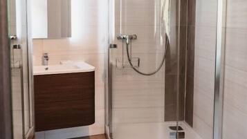 A modern bathroom with a glass-enclosed shower, a white sink, and a dark-toned vanity.
