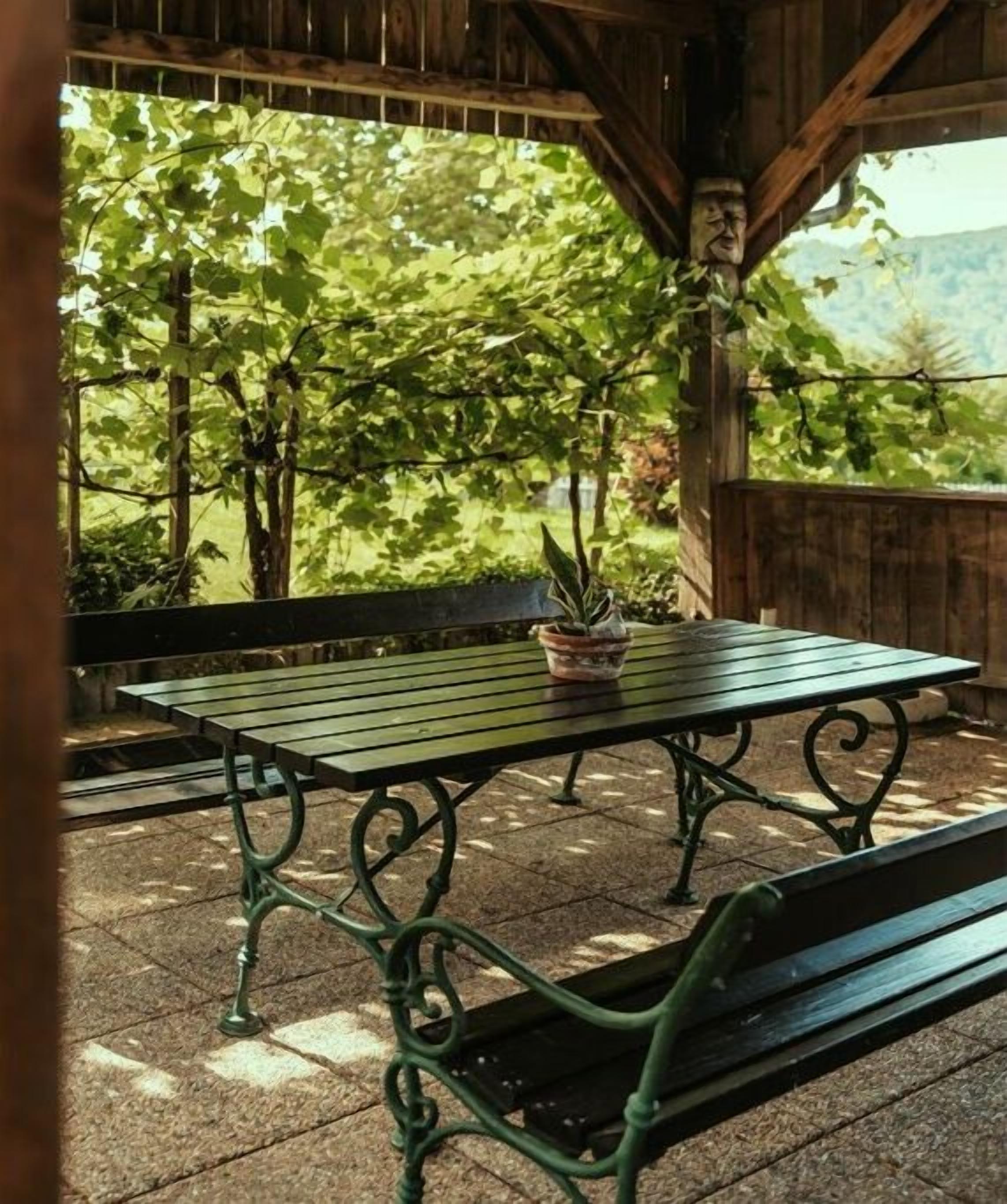 Una struttura in legno all'aperto con tavolo e panchina, immersa nel verde e tra alberi.