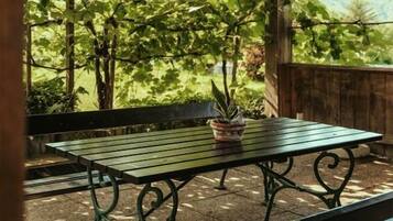 Una struttura in legno all'aperto con tavolo e panchina, immersa nel verde e tra alberi.