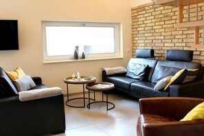 Ein modernes Wohnzimmer mit einem schwarzen Ledersofa, einem braunen Ledersessel und einem kleinen runden Tisch mit Dekoration.