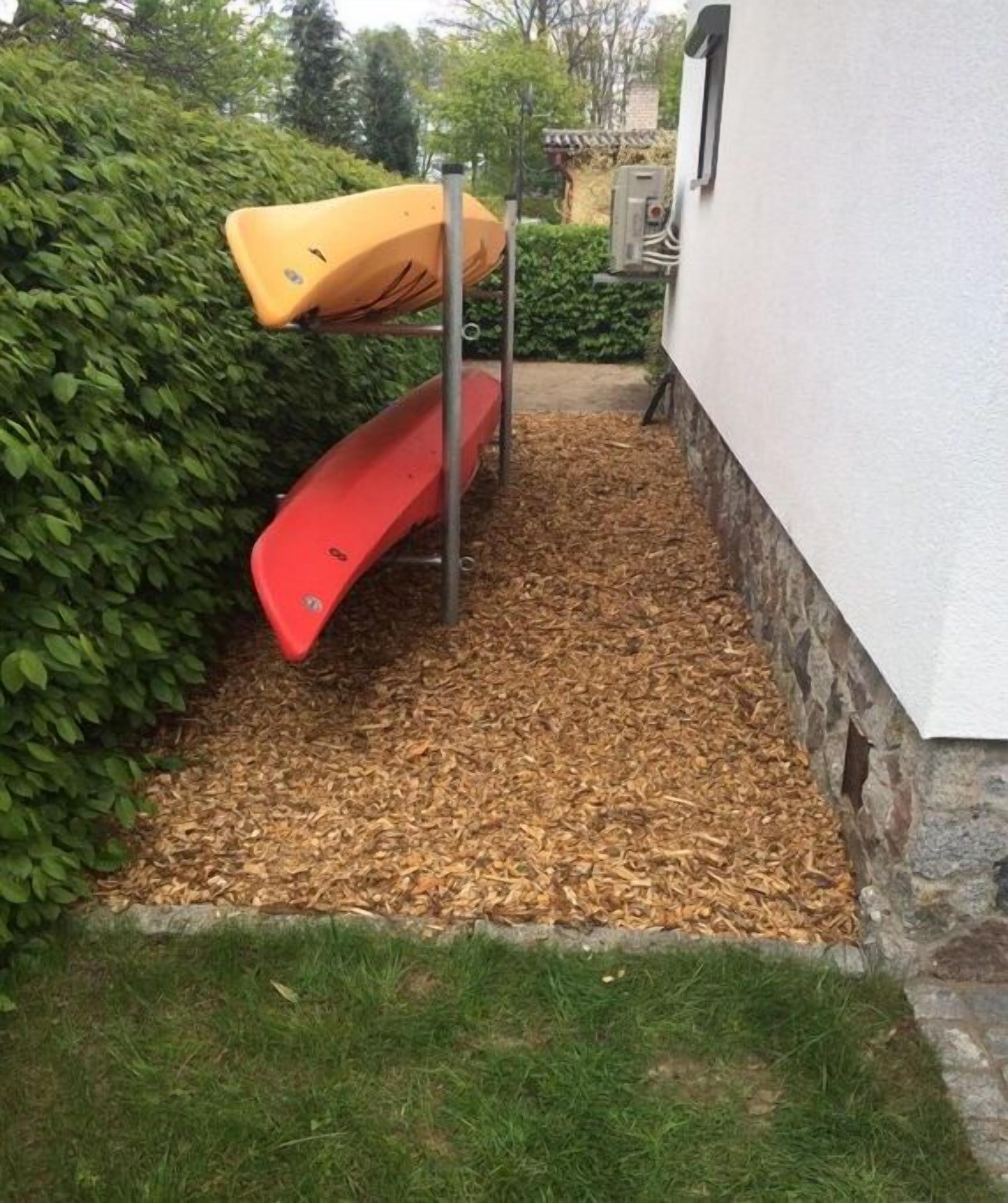 Un espace jardin avec un toboggan rouge et un kayak jaune posé sur un support métallique.