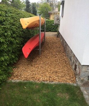 Uma área de jardim com um escorrega vermelho e um caiaque amarelo em um suporte de metal.