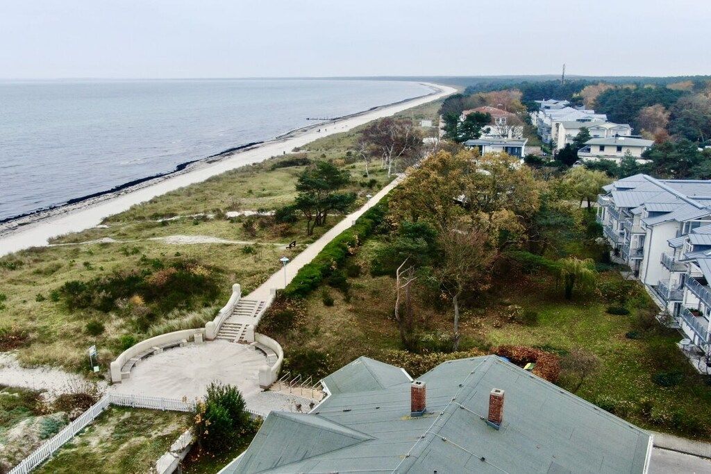 A coastal residential area with a beach, a pathway leading to a circular driveway, and a row of houses with a uniform architectural style.