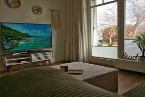 Ein Wohnzimmer mit Fernseher, einem Fenster mit Blick auf Bäume und dem Wort 'Beach' auf dem Fensterbrett.
