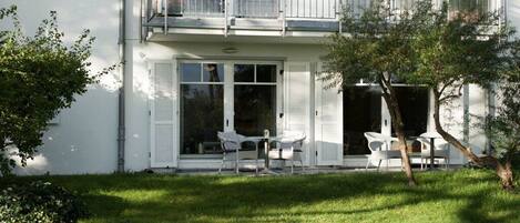 Un bâtiment à deux étages doté d’un balcon, d’un petit patio avec des meubles d’extérieur et d’une pelouse bien entretenue.