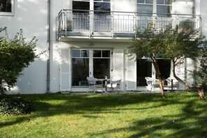 Ein zweistöckiges Gebäude mit einem Balkon, einer kleinen Terrasse und Gartenmöbeln sowie einem gepflegten Rasen.